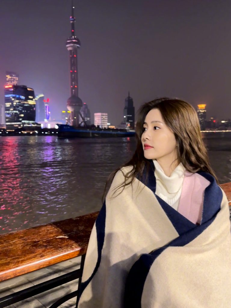 白鹿晒江边美照 披毛毯倚靠围栏侧颜精致 